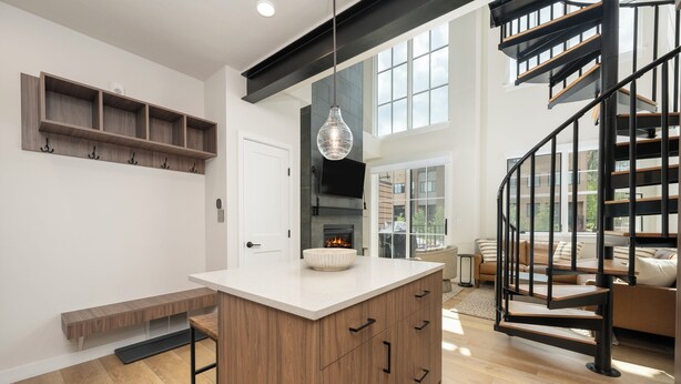 A modern kitchen with a central island, wooden shelving, and a black spiral staircase.