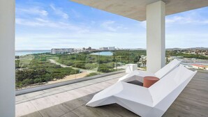 Un balcon moderne offrant une vue dégagée sur un paysage côtier, avec des bâtiments et de la végétation.