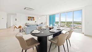 Un espace repas moderne avec une table ronde, quatre chaises et une vue sur la ville grâce à de grandes fenêtres.