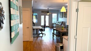 A hallway leading to a dining area with a ceiling fan, a trash can, and a door. - Sandy Dreams, 2-bedroom dog-friendly duplex in Garden City w/fenced yard (Murrells Inlet)