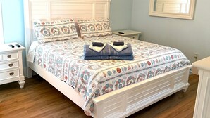 A bedroom with a bed, nightstands, a ceiling fan, a painting, and a mirror. - Sandy Dreams, 2-bedroom dog-friendly duplex in Garden City w/fenced yard (Murrells Inlet)