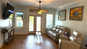 A spacious living room with a leather sofa, a small round table, and a ceiling fan. - Sandy Dreams, 2-bedroom dog-friendly duplex in Garden City w/fenced yard (Murrells Inlet)