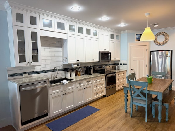 A modern kitchen with white cabinetry, stainless steel appliances, and a wooden dining table.