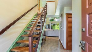 A staircase with wooden steps and a green handrail, leading to a room with a sofa and a window. - Princeville Island Charm Townhome - Puamana 19C (Princeville)