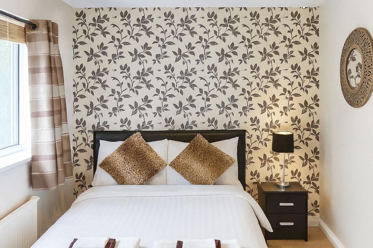 Een netjes ingerichte slaapkamer met een bed, nachtkastjes, een lamp en een decoratieve spiegel.