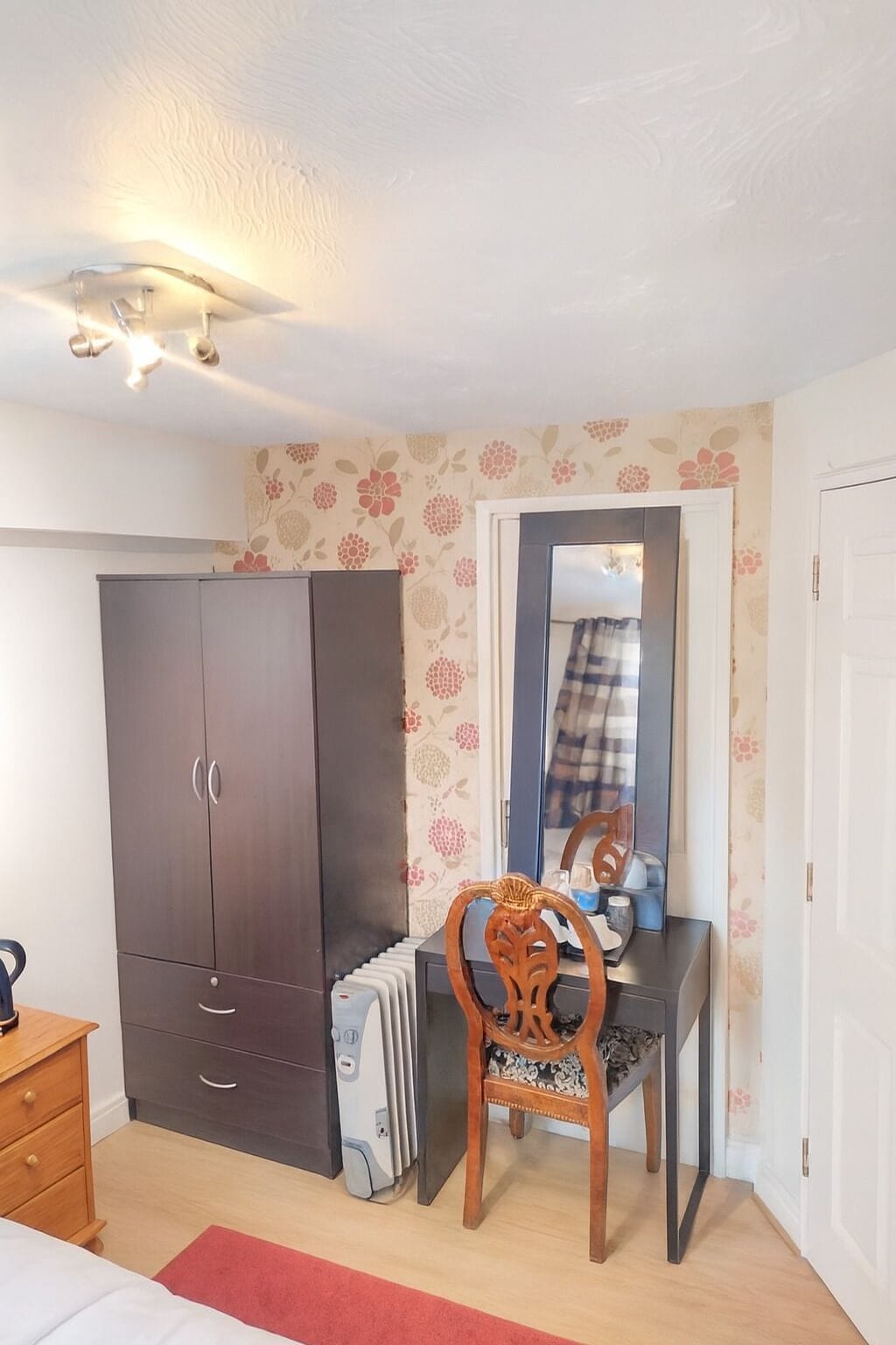 A bedroom with a wardrobe, a desk with a chair, a radiator, and a mirror.
