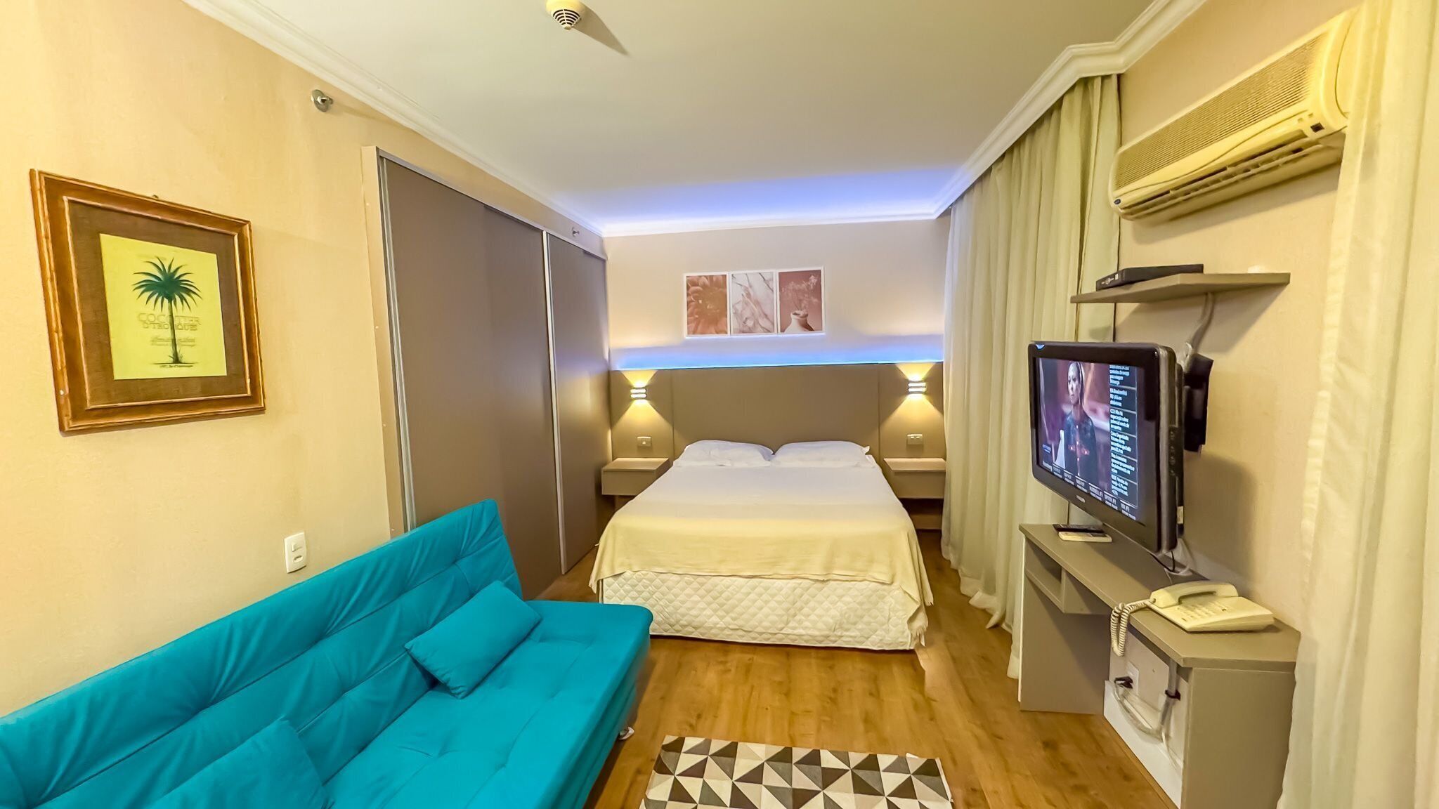Une chambre d’hôtel avec un lit, un canapé bleu, une télévision et un bureau avec un téléphone.