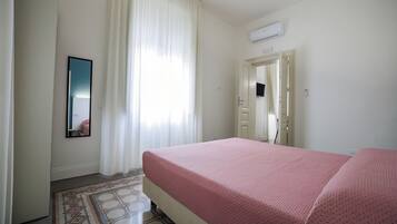 Habitación de hotel con cama, espejo, puerta y ventana con cortinas.