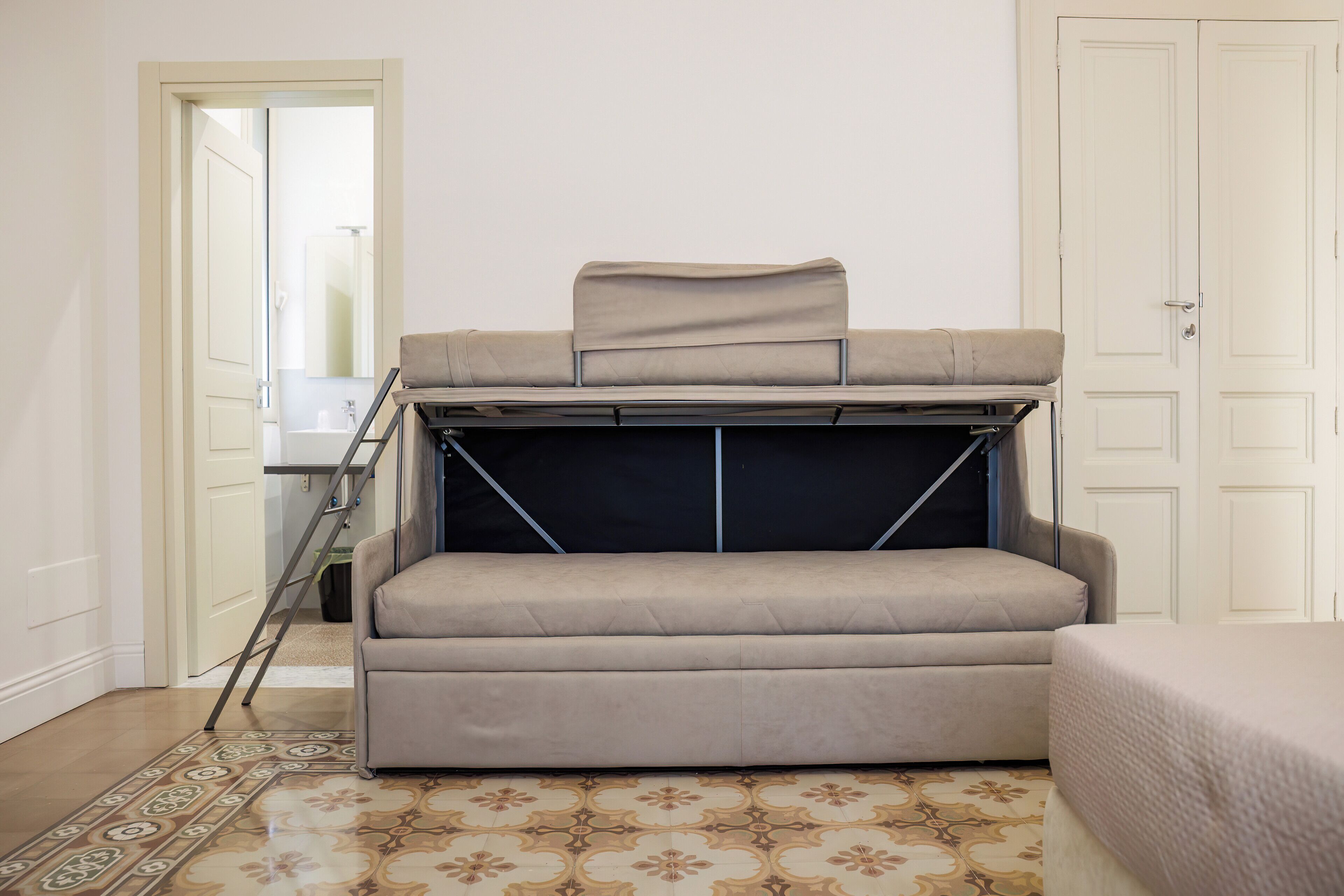 Habitació compacta amb un sofà llit plegable, una finestra petita i una porta que dona a un bany.