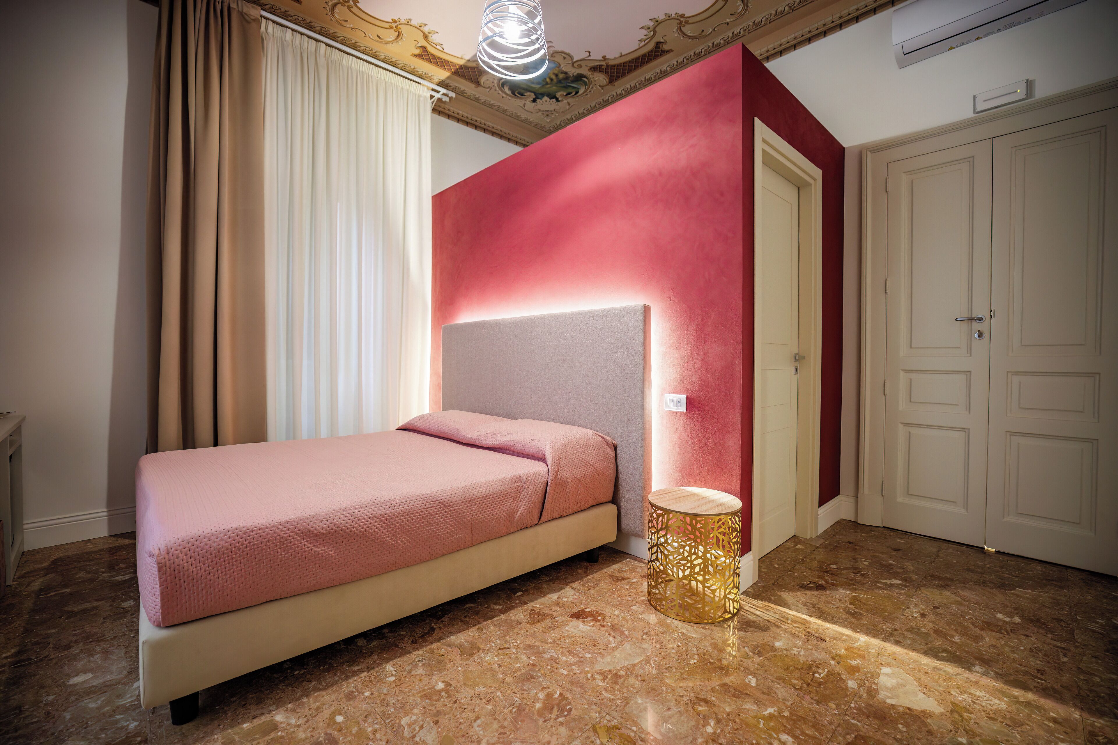 A bedroom with a bed, a round side table, a door, and a red accent wall.