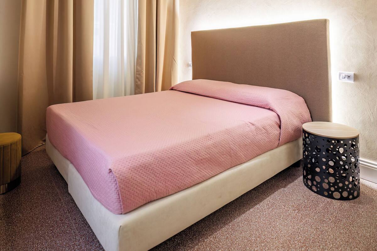Hotellihuone, jossa on sänky, verhot, pyöreä pöytä ja koristeellinen kuviointi katossa.