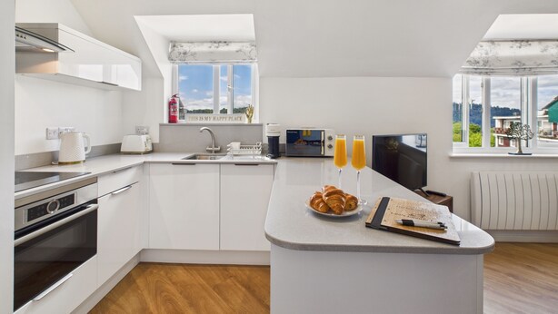 Une cuisine moderne avec des meubles blancs, un îlot central et une vue sur l’extérieur grâce à de grandes fenêtres.