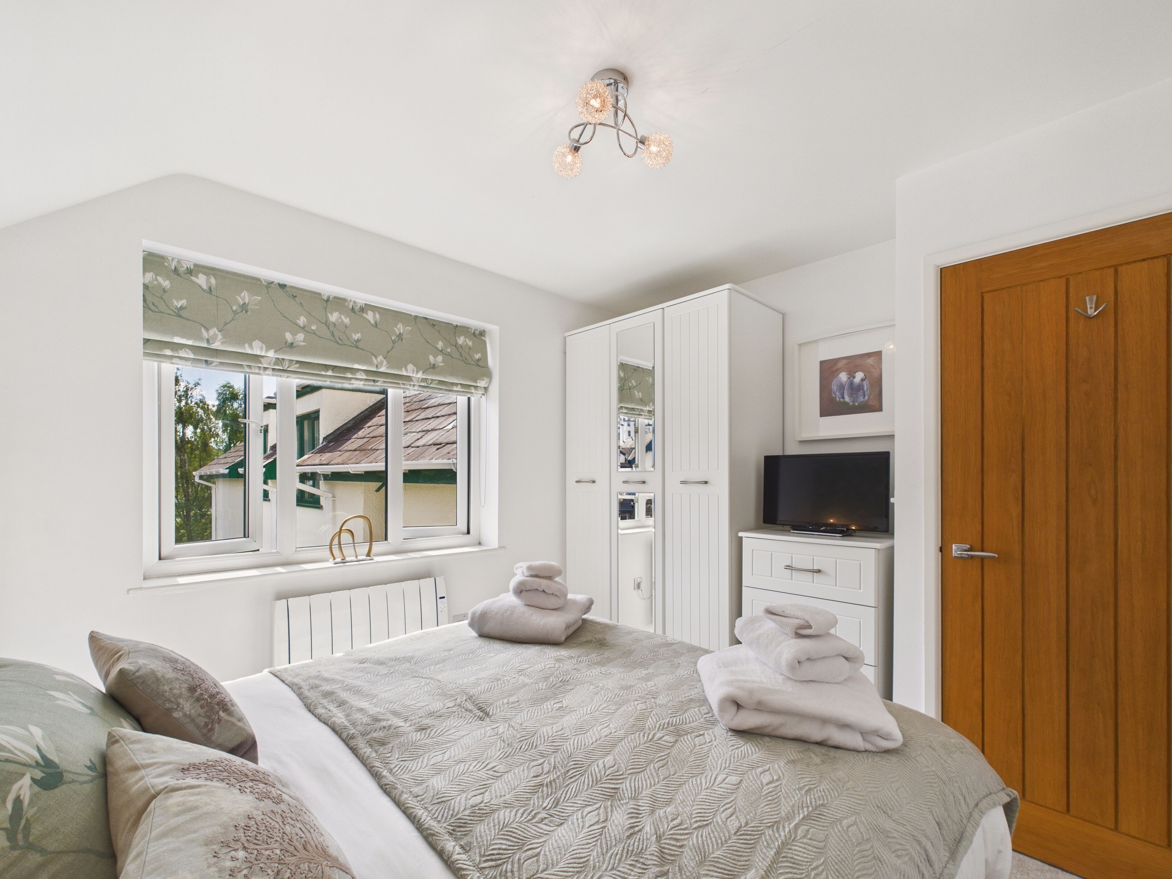 Een slaapkamer met een bed, een kledingkast, een televisie en een raam met uitzicht op een huis.