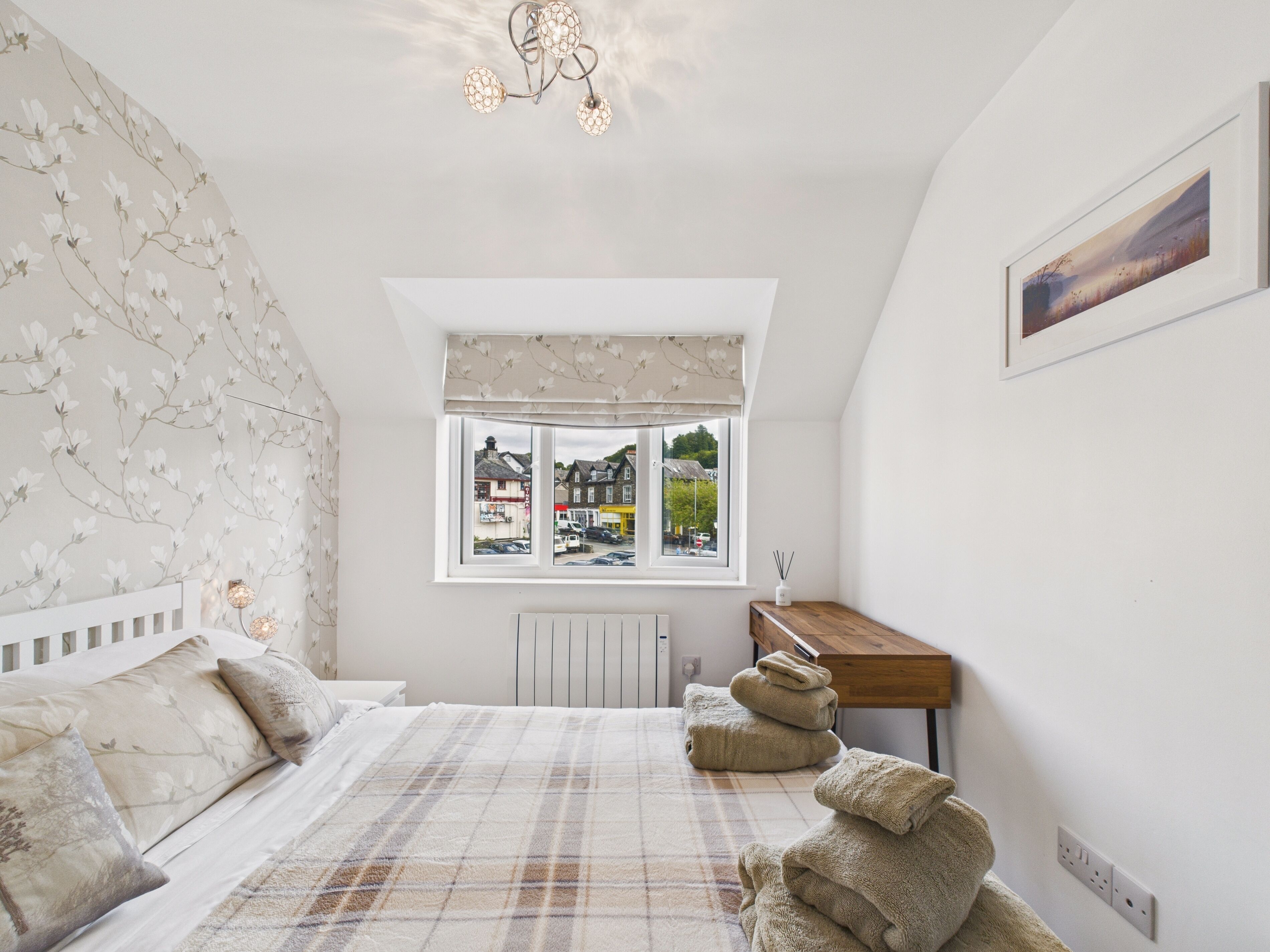Une chambre à coucher avec un lit, une fenêtre donnant sur des immeubles, un radiateur et une table de chevet avec une lampe.