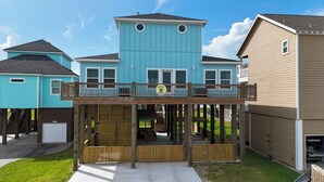 A two-story house with a balcony, a garage, and a covered outdoor seating area. - Casa de Tortuga: 4  BR, 3  BA House in Crystal Beach, Sleeps 12 (Bolivar Peninsula)