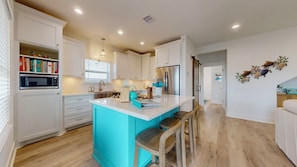 Une cuisine moderne avec des meubles blancs, un îlot de couleur turquoise et des chaises en bois.