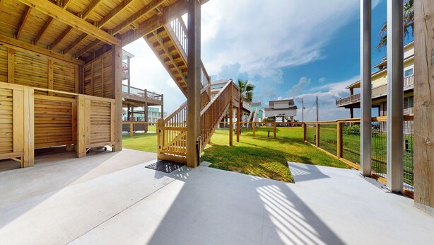 A wooden structure with a covered patio, a grassy area, and a view of a building with multiple balconies. - Casa de Tortuga: 4  BR, 3  BA House in Crystal Beach, Sleeps 12 (Bolivar Peninsula)
