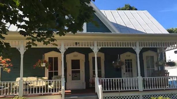 Une maison verte avec un porche blanc et des portes numérotées.