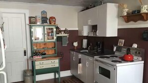 Une cuisine compacte équipée d’une cuisinière, d’un évier et d’un meuble vert avec des étagères ouvertes.