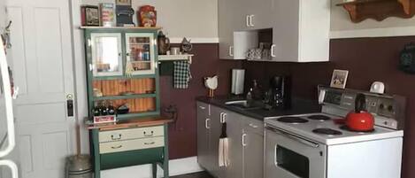 A compact kitchen with a stove, sink, and a green cabinet with open shelves.