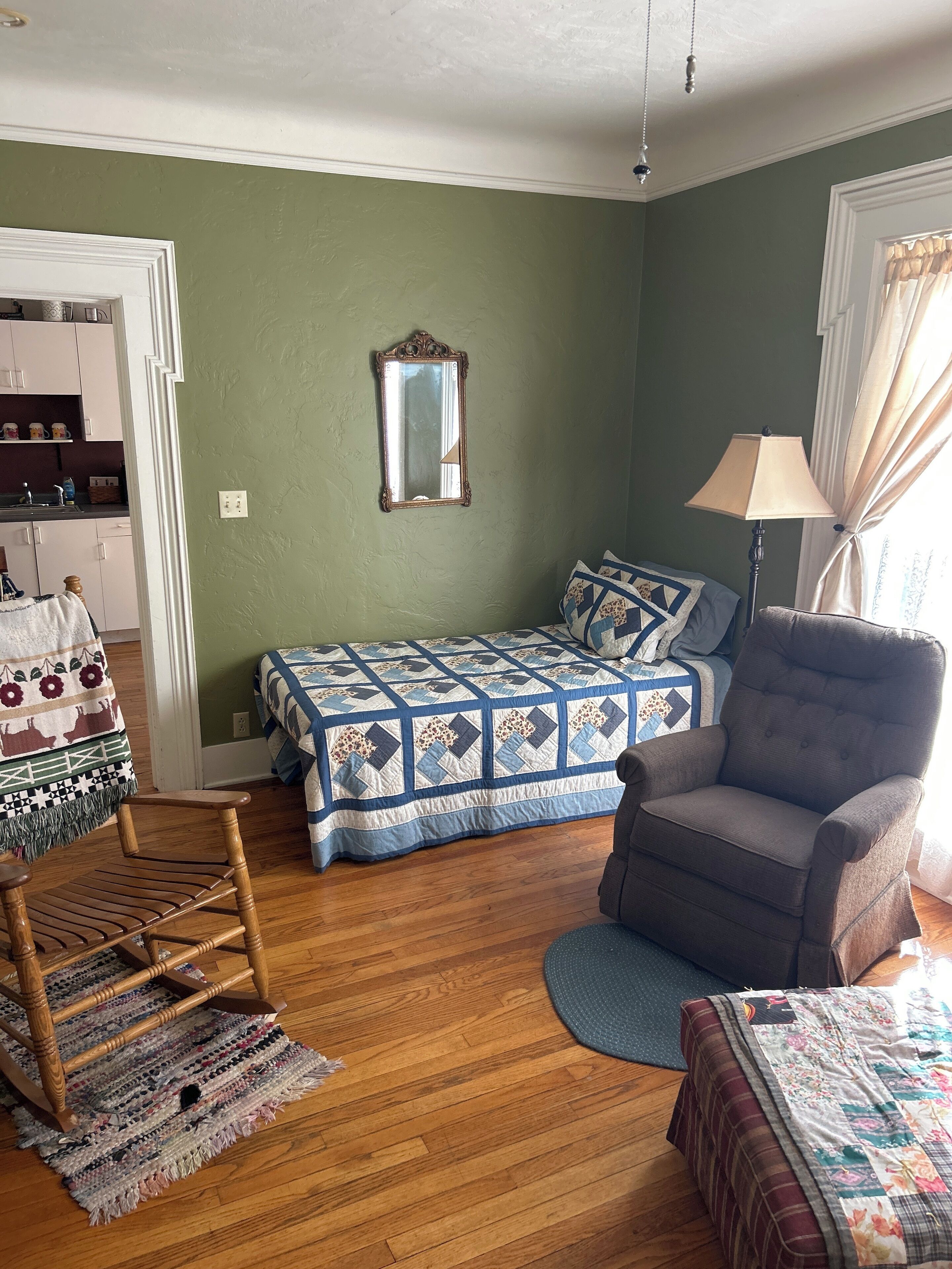 A bedroom with a bed, a chair, a rug, and a dresser.