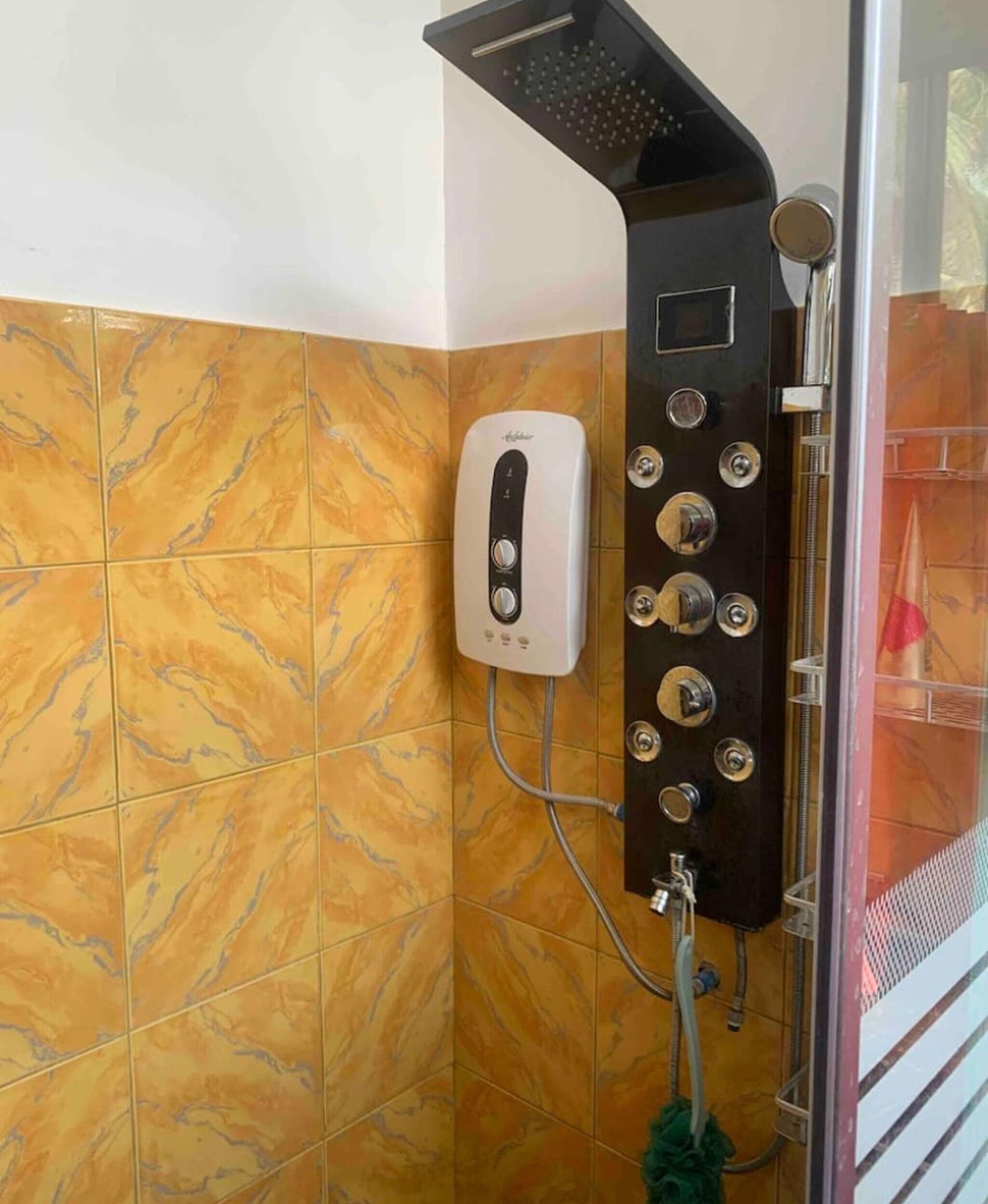 A shower with a control panel, a handheld showerhead, and a handheld scrubber.
