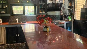 A modern kitchen with a central island, black cabinets, and hanging pots.