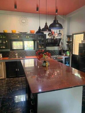 A modern kitchen with a central island, black cabinets, and hanging pots. - Spacious Beachfront House With Rooftop Deck in Macrohon, Philippines (Macrohon)