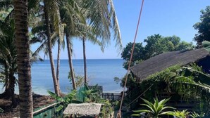 A balcony with a view of the ocean, surrounded by palm trees and a thatched-roof structure.