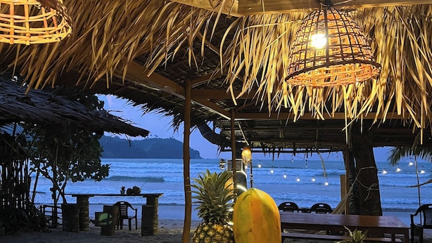 A beachside restaurant with a thatched roof, wooden tables, and a view of the ocean. - Bucana Beach House North El Nido (El Nido)