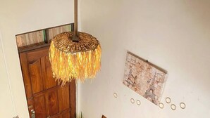A room with a wooden sofa set, a coffee table, a dining table with blue plates, and a hanging light fixture. - Bucana Beach House North El Nido (El Nido)