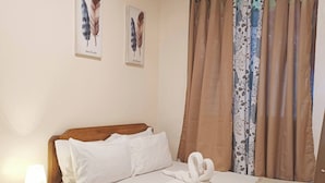 A neatly made bed with white linens, a bedside table with a lamp, and two feather wall art pieces. - Bucana Beach House North El Nido (El Nido)