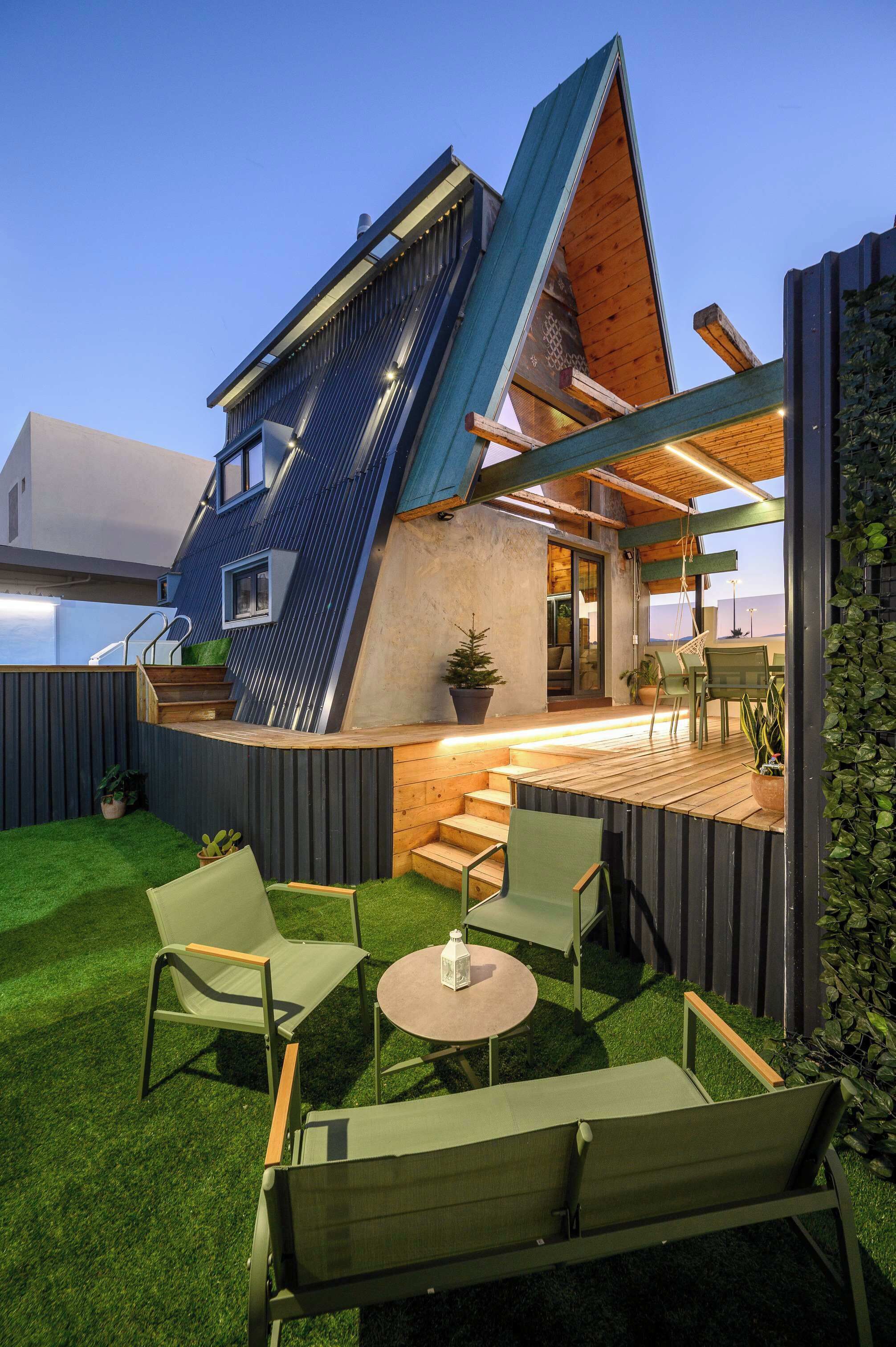 A modern house with a sloped roof, a deck with outdoor furniture, and a small garden.