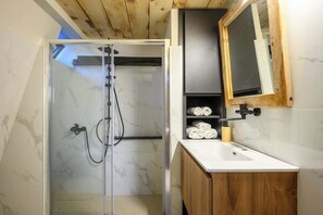 Een moderne badkamer met een glazen douchecabine, marmeren tegels, houten kasten en een ingebouwd wastafelmeubel.