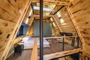 A cozy attic bedroom with a sloped ceiling, wooden walls, a bunk bed, a desk, and a window.