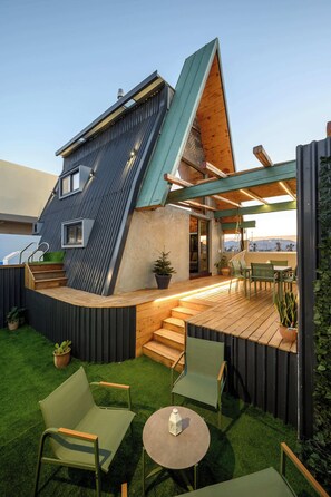 Een modern huis met een schuin dak, een houten terras en buiten zitplaatsen.