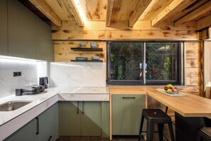 A modern kitchen with wooden ceiling beams, a marble countertop, a sink, and a window with blinds. - A-Home Villa, Private Pool & Jetted Tub Oasis (Nea Alikarnassos)