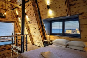 Een houten kamer met een slaapzolder, een klein bureau en een raam met zonwering.