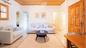 A living room with a wooden ceiling, a white sofa, a round coffee table, and a wooden door.