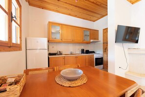 Una cocina con armarios de madera, un refrigerador, una estufa y un televisor instalado en la pared.