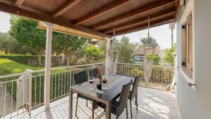 An outdoor patio with a table and chairs, a hanging light fixture, and a view of a garden and buildings.
