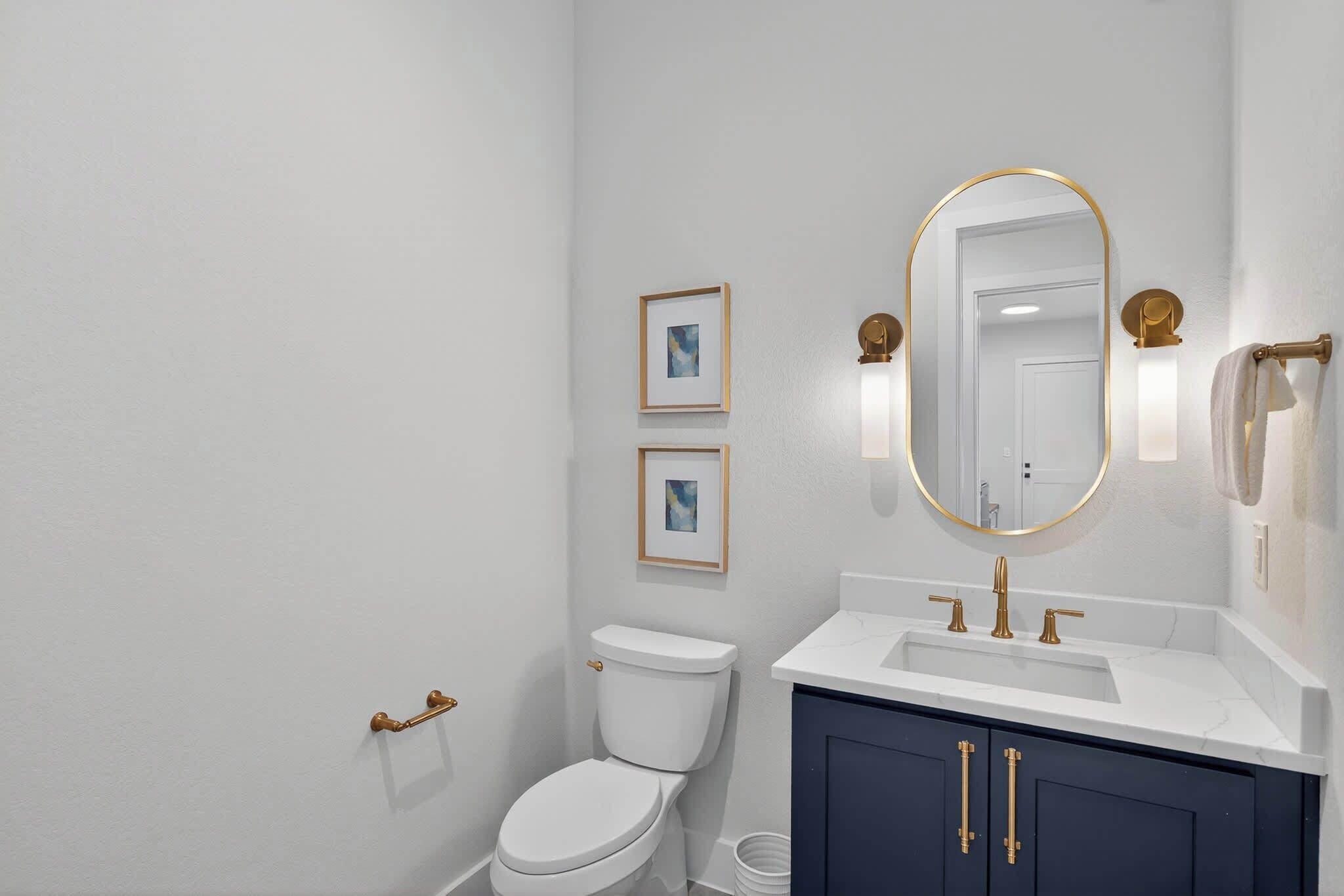A bathroom with a white toilet, a vanity with a gold faucet, and two framed pictures on the wall.