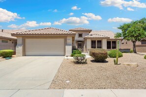 A residential house with a garage, a small porch, and a well-maintained garden with gravel and plants. - Beautiful home in the Grand very desirable for snow birds, come relax and enjoy (Surprise)