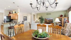 A modern kitchen with wooden cabinets, a dining table with chairs, and a chandelier.