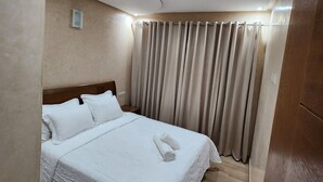 Ein Hotelzimmer mit einem ordentlich bezogenen Bett, einem Holzkopfteil, einem Holzboden und einem Vorhang, der das Fenster verdeckt.