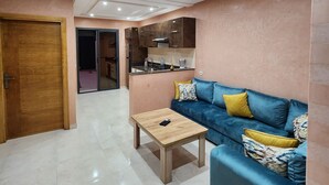 Ein modernes Wohnzimmer mit einem blauen Sofa, einem Holztisch und einer Küchenzeile im Hintergrund.