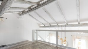 An empty room with a sloped ceiling, wooden beams, and a large window with a view of buildings. - Casa del Borgo by Wonderful Italy (Bologna)