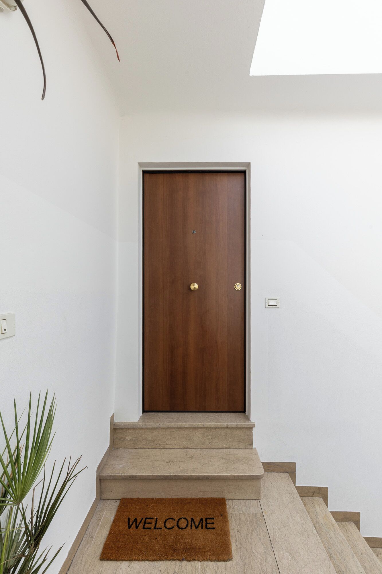 A wooden door with a brass handle and a doorknob, leading to a staircase with a 'WELCOME' mat.