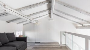 A modern loft with exposed wooden beams, a grey sofa, and a view of the city through large windows. - Casa del Borgo by Wonderful Italy (Bologna)