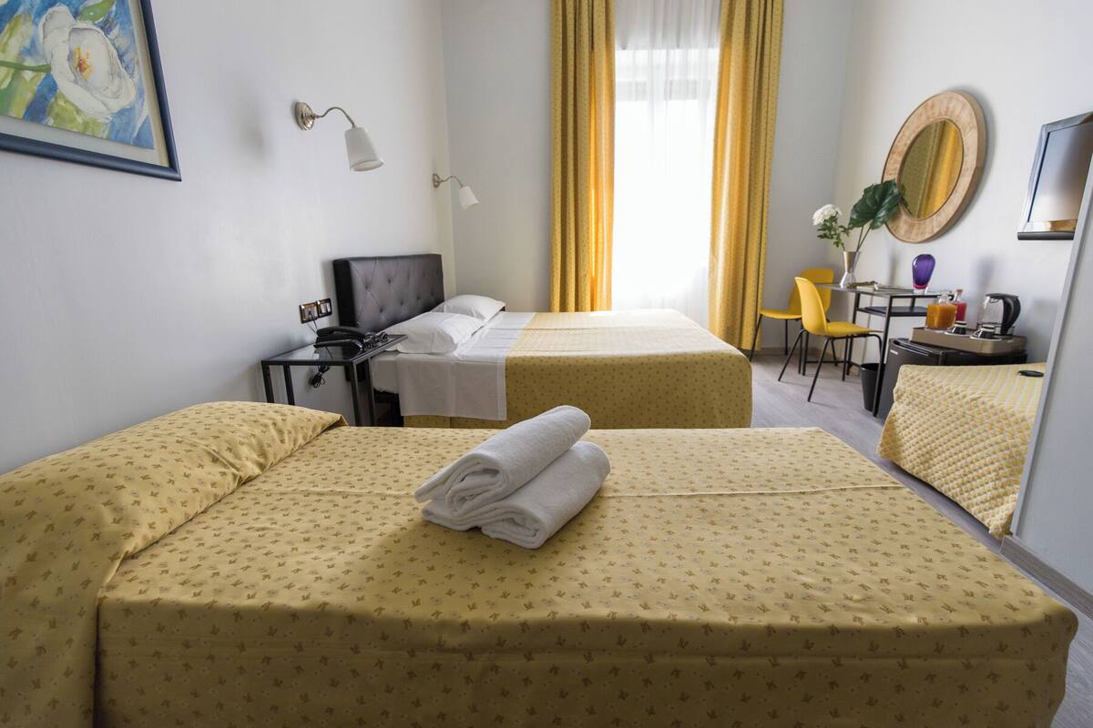 A hotel room with two beds, a desk, a chair, a TV, and a painting on the wall.